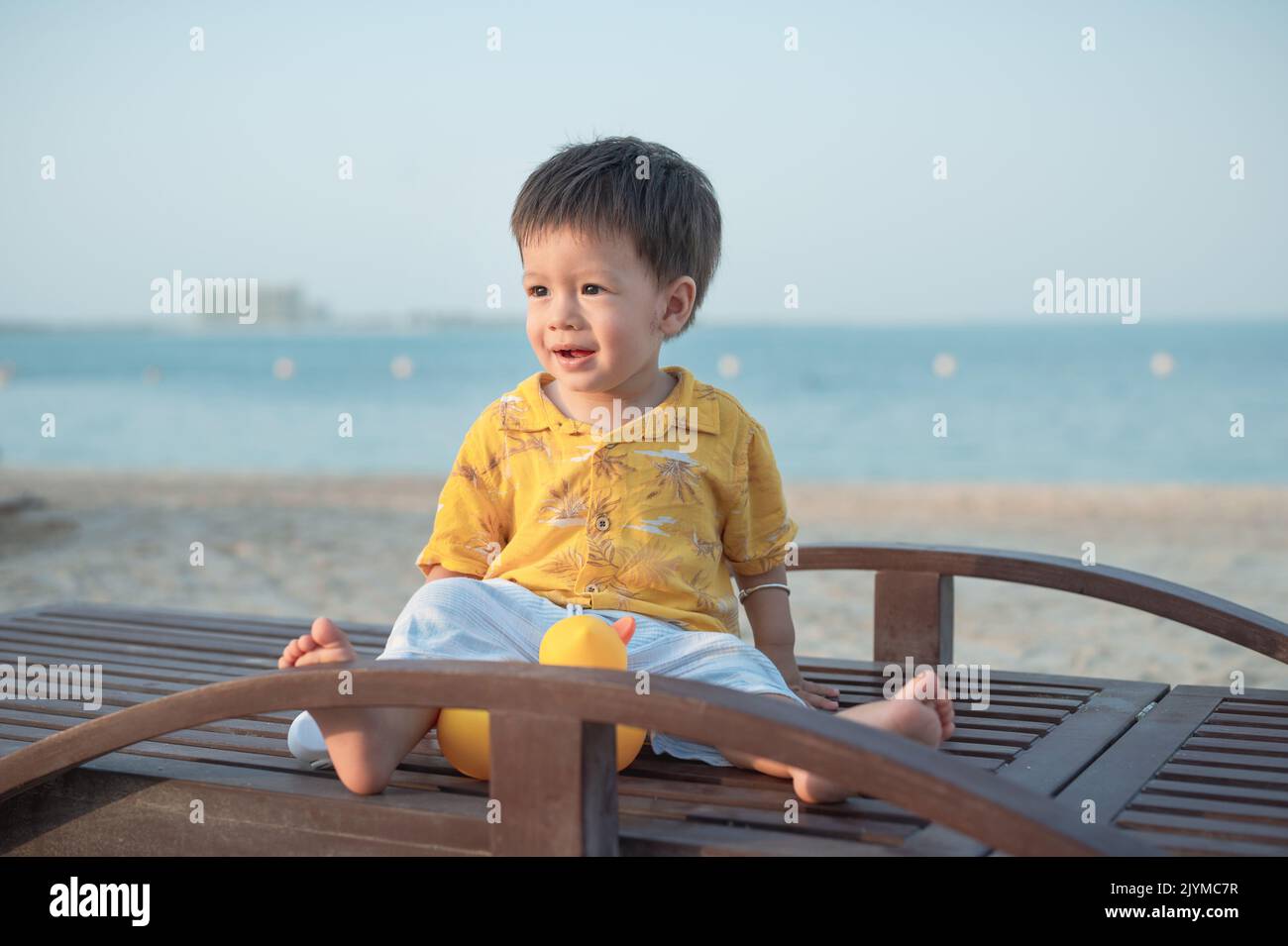 Bébé garçon sur une plage de vacances assis sur le transat au coucher du soleil. Un enfant d'un an de sexe masculin en vacances au bord de la mer assis sur le transat Banque D'Images