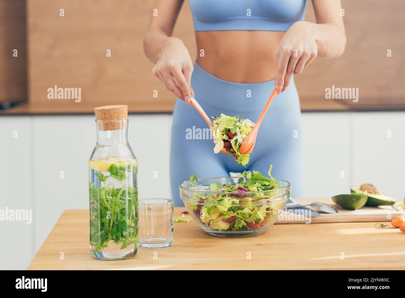 Gros plan photo, partie du corps, mains de la jeune femme de forme physique qui fait de la salade avec des légumes frais et de la boisson fraîche de détox dans la cuisine à la maison Banque D'Images