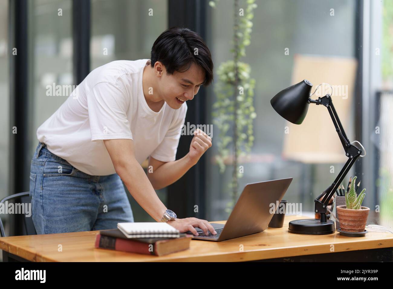 Un homme asiatique heureux utilisant un ordinateur portable tout en ayant une bonne nouvelle de travailler au bureau Banque D'Images