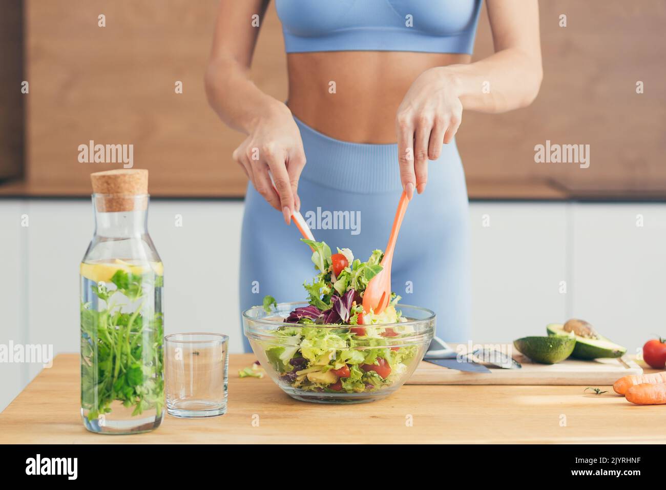Gros plan photo, partie du corps, mains de la jeune femme de forme physique qui fait de la salade avec des légumes frais et de la boisson fraîche de détox dans la cuisine à la maison Banque D'Images