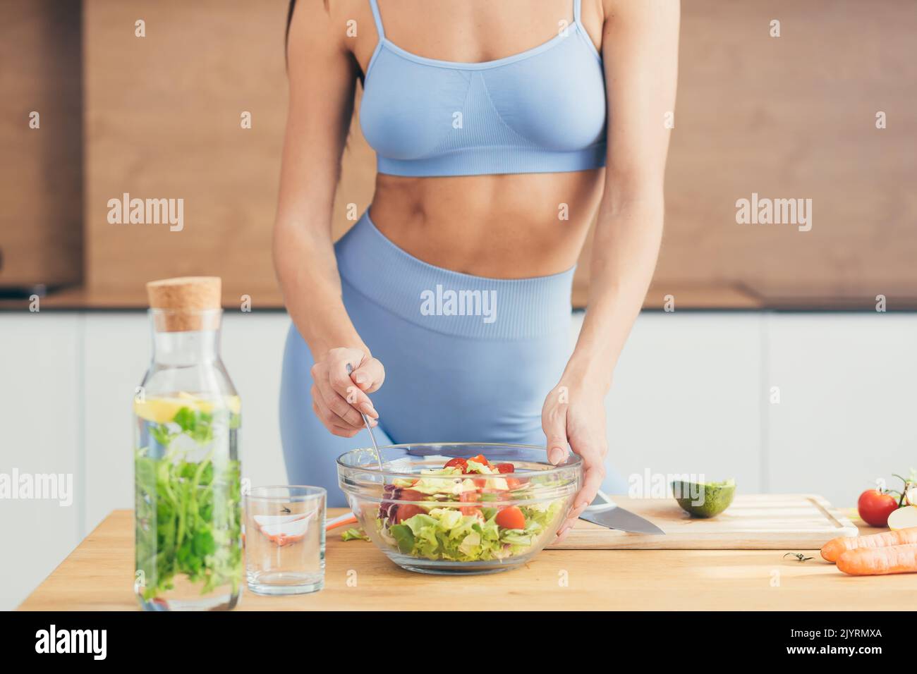 Gros plan photo, partie du corps, mains de la jeune femme de forme physique qui fait de la salade avec des légumes frais et de la boisson fraîche de détox dans la cuisine à la maison Banque D'Images