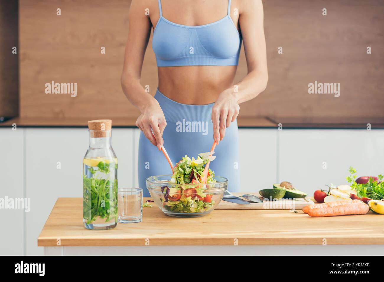 Gros plan photo, partie du corps, mains de la jeune femme de forme physique qui fait de la salade avec des légumes frais et de la boisson fraîche de détox dans la cuisine à la maison Banque D'Images