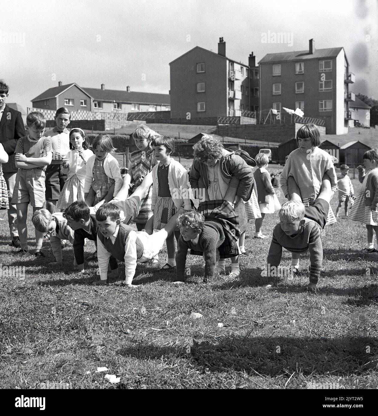 1965, historique, n. queensferry gala jour, les enfants prêts à commencer une activité amusante, une course de roussets à l'extérieur sur l'herbe dans un champ d'un domaine de logement à North Queensferry, Fife, Écosse, Royaume-Uni, les jeunes filles braves tenant les jambes des garçons! Banque D'Images