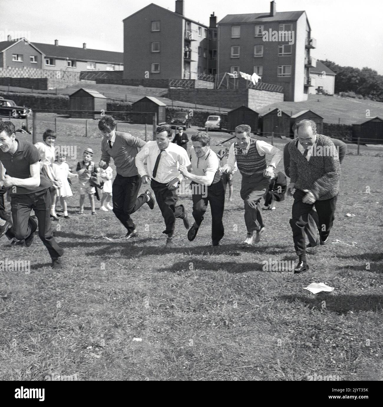 1965, hommes adultes historiques participant à une compétition de course dans un champ dans un domaine d'habitation à North Queensferry, Fife, Écosse, Royaume-Uni, dans le cadre de la journée de gala de North Queensferry, une journée d'activités communautaires pour les résidents. Banque D'Images