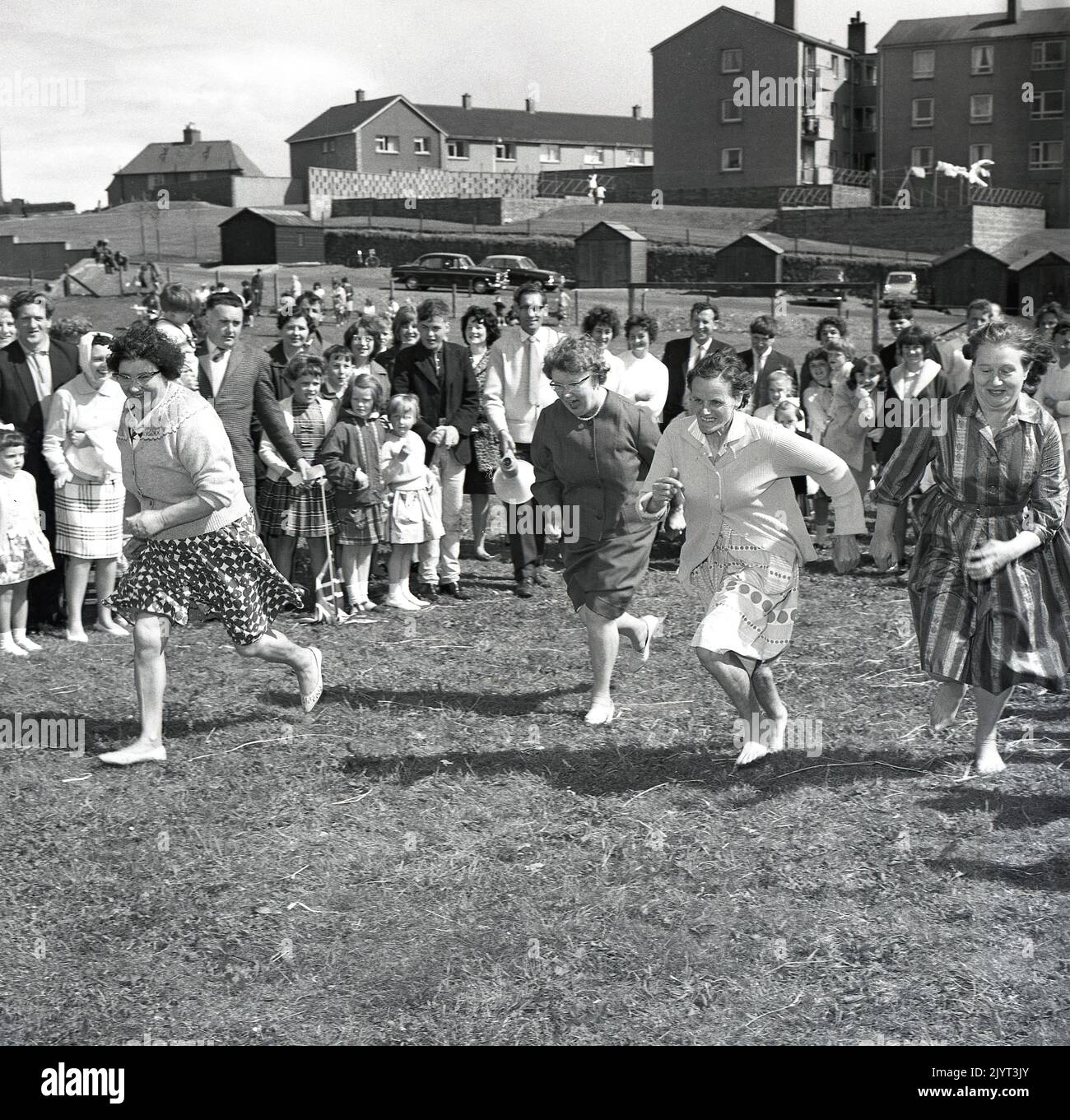 1965, historique, les femmes prenant part à une compétition de course, deux dans les pieds de bareft, sur l'herbe dans un champ dans un domaine de logement à North Queensferry, Edimbourg, Ecosse, Royaume-Uni, dans le cadre de la journée de gala de North Queensferry. Banque D'Images