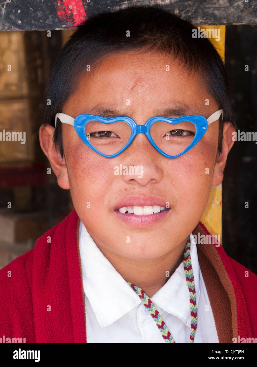 Portrait d'enfant local / enfant d'héritage tibétain portant des vêtements bouddhistes et aussi des lunettes de fantaisie avec un cadre en forme de deux coeurs, une personne qui vit en Chine, résident d'un petit village à l'extérieur de la ville antique de Songpan dans le nord de la province du Sichuan. PRC. Chine (126) Banque D'Images