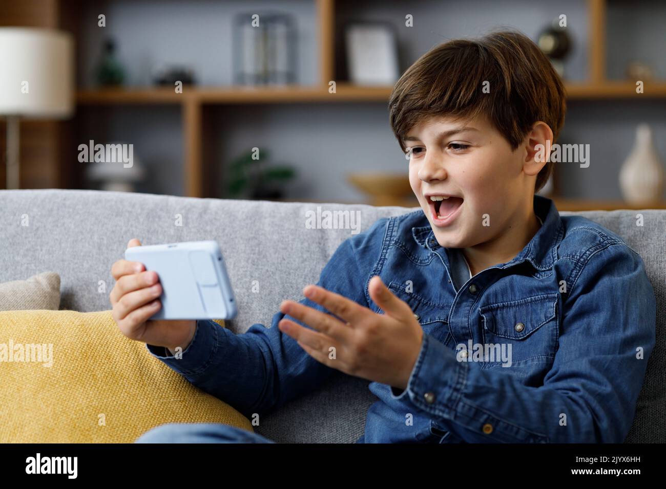 Le jeune garçon réagit émotionnellement à ce qui se passe sur l'écran du smartphone. Adolescent passant du temps chez lui avec un gadget numérique. Adolescence et Banque D'Images