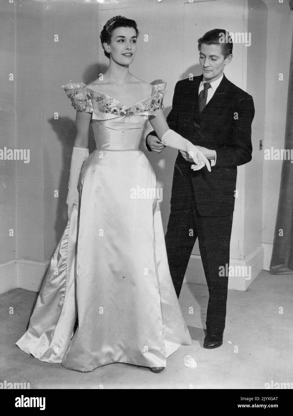 Robert Schulz, designer australien de Boolaroo, Adélaïde, avec l'un des modèles qu'il a conçus pour sa collection londonienne. Deux robes de soirée de son spectacle ont été sélectionnées pour la collection de la tournée royale qui sera envoyée en Australie. Le couturier australien Robert Schulz, de Booleroo, Adélaïde, avec l'un des modèles de sa première collection, qui a reçu l'acclamation lorsqu'il a été présenté à Londres la semaine dernière. 'Jersey Lily' est une robe de couronnement en satin blanc avec un ***** formé par cannelé ***** panneau. Collier et ***** sont brodés d'or. 27 janvier 1953. Banque D'Images