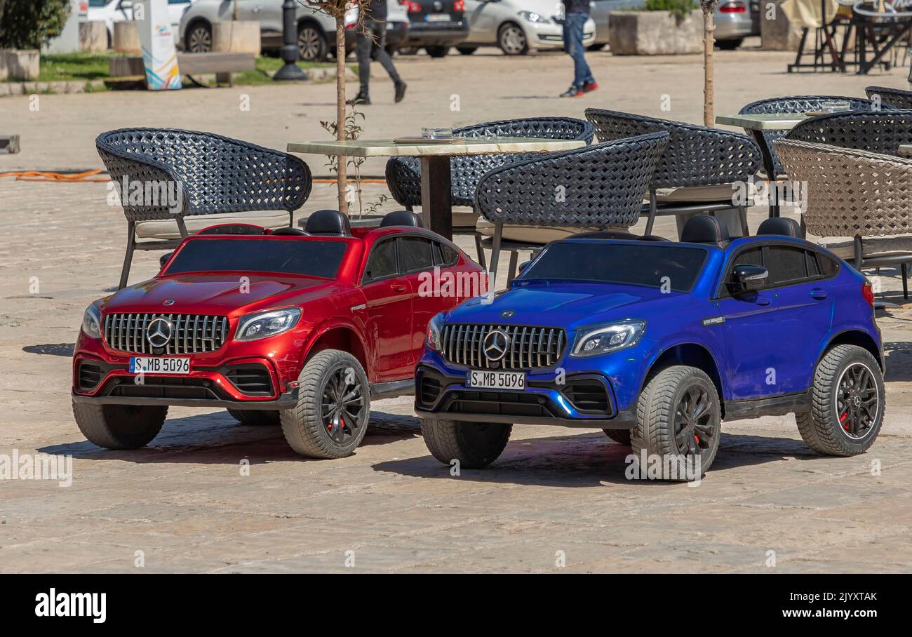 Budvar, Monténégro- 26 avril 2022 -deux jouets miniatures Mercedes pour enfants garés dans le port par quelques chaises de jardin Banque D'Images