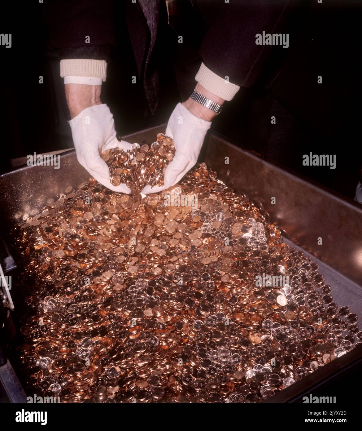 1971: Photo de dossier datée de février 1971 d'un ouvrier à la monnaie royale de Llantrisant, au sud du pays de Galles, mettant ses mains gantées dans une masse de pièces de clôture en cuivre nouvellement taillées. Date de publication : jeudi 8 septembre 2022. Banque D'Images