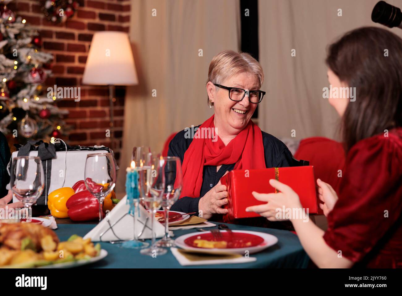 Famille échangeant des cadeaux de noël à la table, célébrant les vacances d'hiver, ayant un dîner de fête, manger des plats traditionnels. Fête de Noël avec les parents, fille donnant maman cadeau boîte Banque D'Images