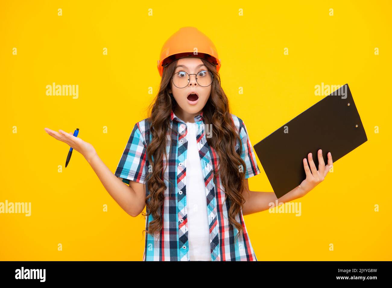 Une adolescente surprise choquée. Enfant peintre adolescent dans un casque avec presse-papiers. Enfant dans un casque de sécurité. Un ingénieur enfant sur le chantier. Rénovation et Banque D'Images