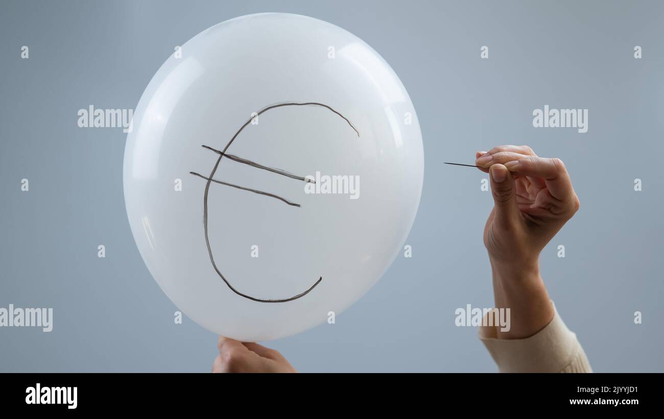 Une femme éclate avec une aiguille un ballon avec l'inscription euro. Banque D'Images