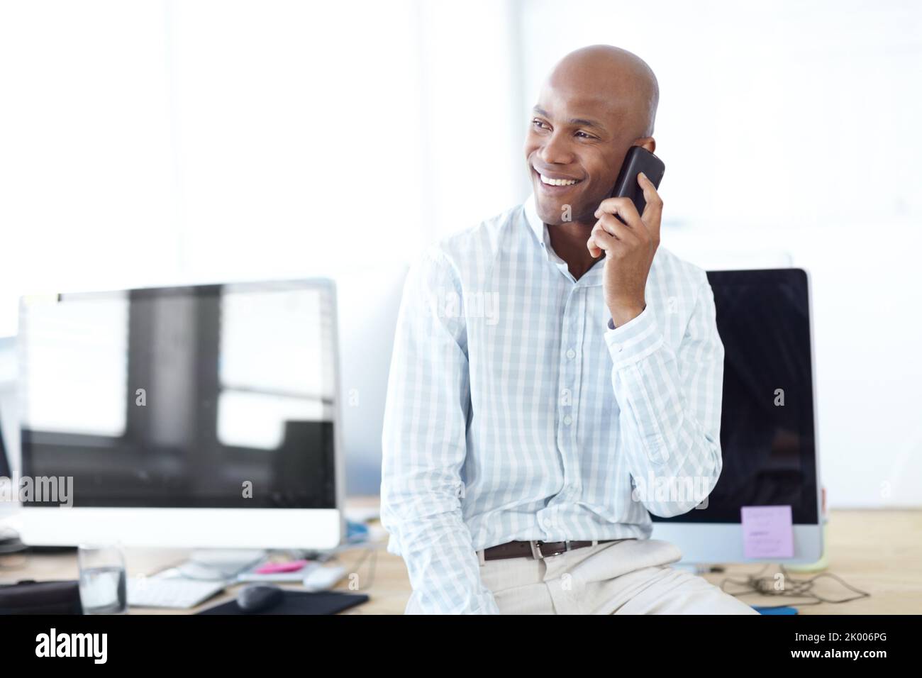 Contacter de vieux associés d'affaires. Un jeune homme d'affaires parlant au téléphone tout en étant assis sur un bureau bordé d'ordinateurs. Banque D'Images