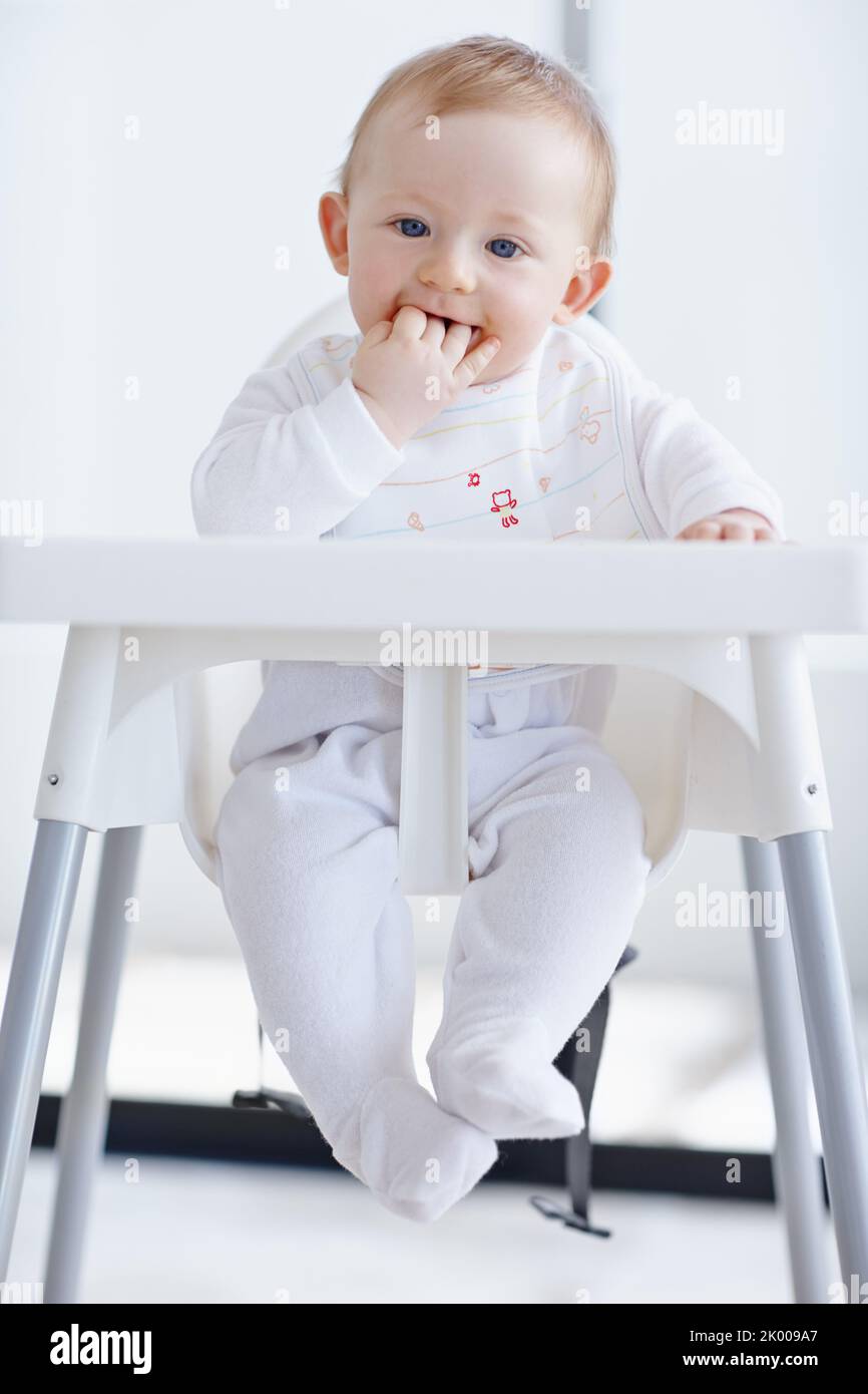 En attente de maman pour me nourrir. Un joli petit garçon dans sa chaise haute avec ses doigts dans sa bouche. Banque D'Images