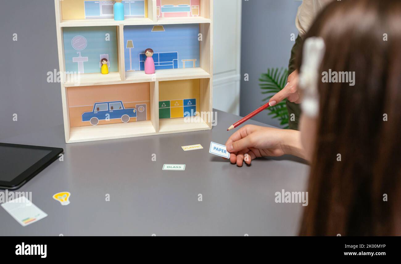 Professeur méconnaissable enseignant le recyclage avec une maison de jouets à une étudiante dans une classe d'écologie Banque D'Images