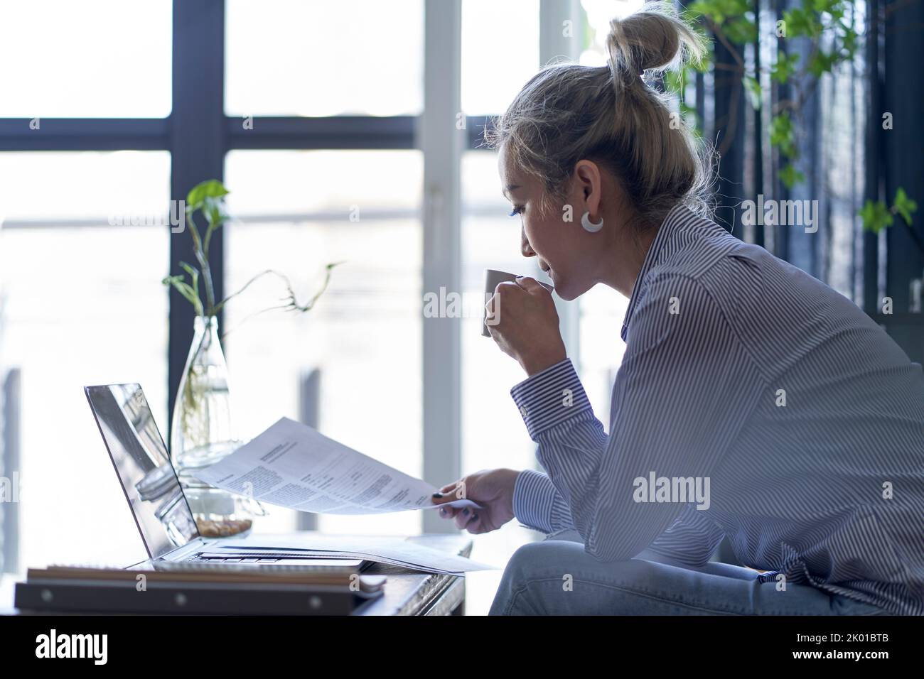 femme asiatique professionnelle mature travaillant à domicile à l'aide d'un ordinateur portable tout en regardant un document papier, vue latérale Banque D'Images femme asiatique professionnelle mature travaillant à domicile à l'aide d'un ordinateur portable tout en regardant un document papier, vue latérale Banque D'Images