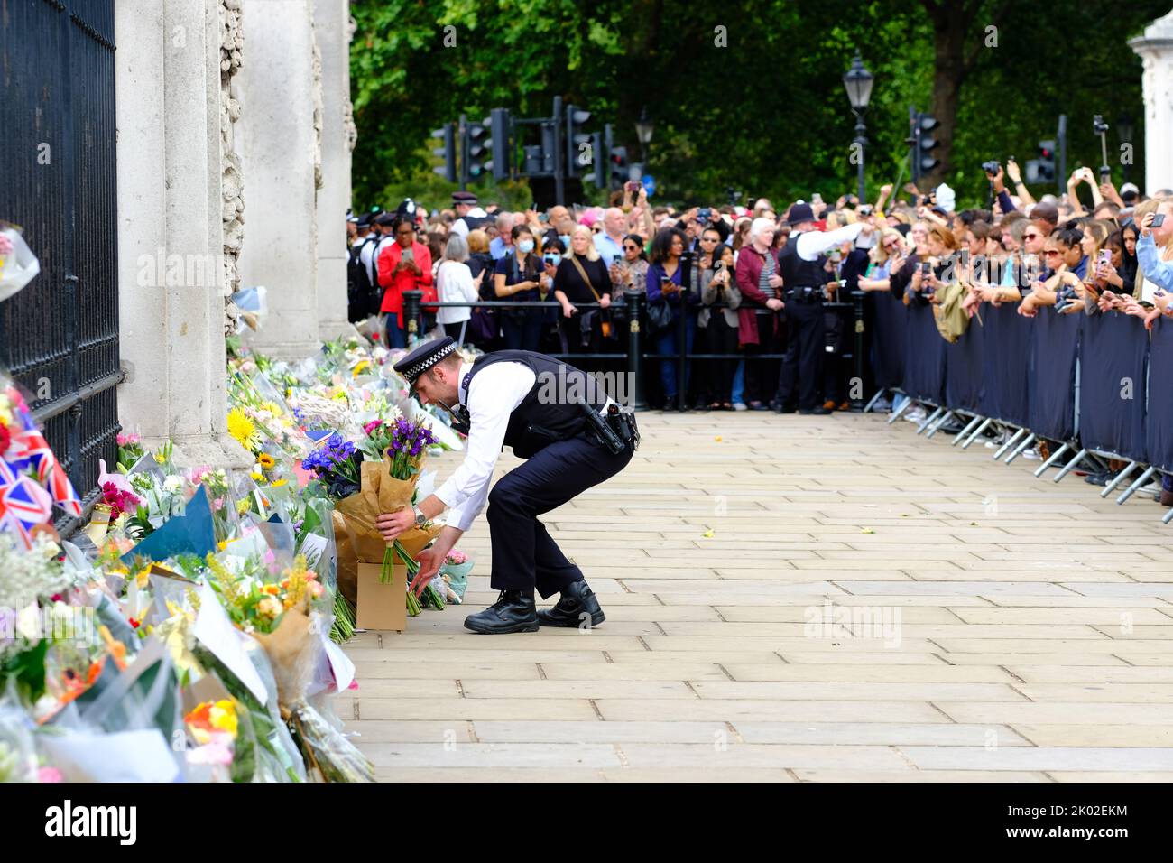 Buckingham Palace, Londres, Royaume-Uni – vendredi 9th septembre 2022 – Un policier dépose des fleurs transmises par la grande foule devant Buckingham Palace alors que le public pleure la mort de la reine Elizabeth II hier. Photo Steven May / Alamy Live News Banque D'Images