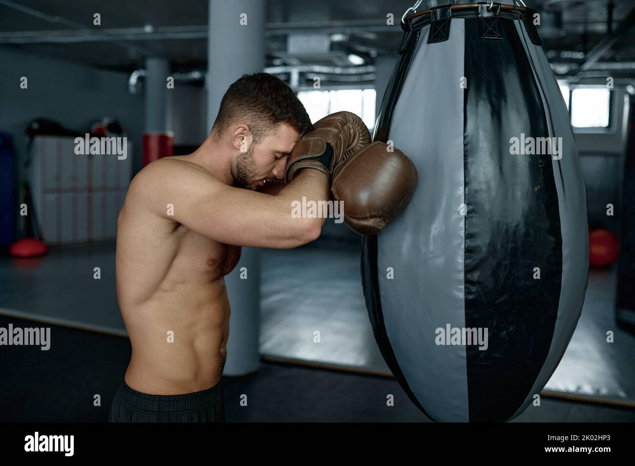Boxeur fatigué tenant un sac de poinçonnage en pleine fatigue Banque D'Images