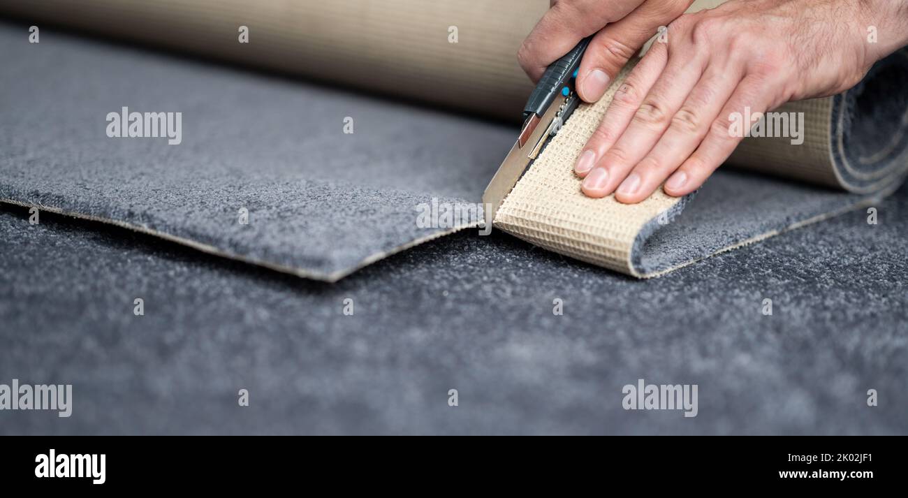 Un homme de main coupe un nouveau tapis avec un couteau à moquette. Banque D'Images