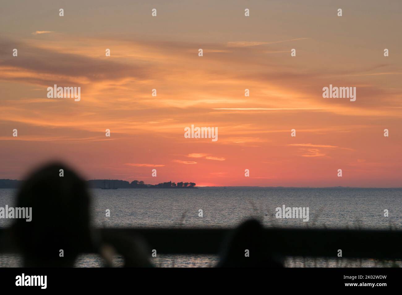 Un homme avec un téléphone portable regarde le coucher de soleil sur la mer. Banque D'Images