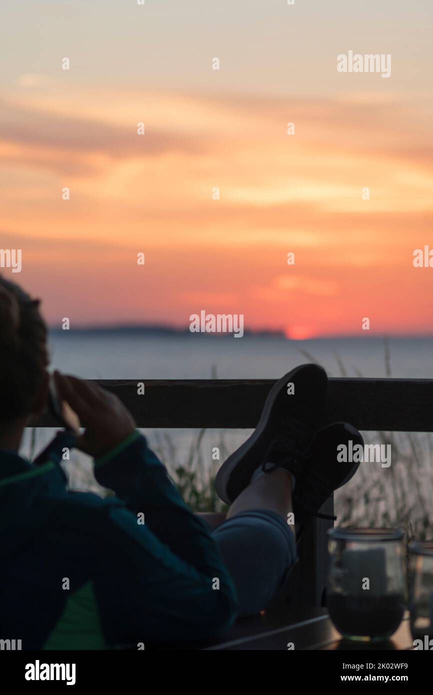 Un homme avec un téléphone portable regarde le coucher de soleil sur la mer. Banque D'Images