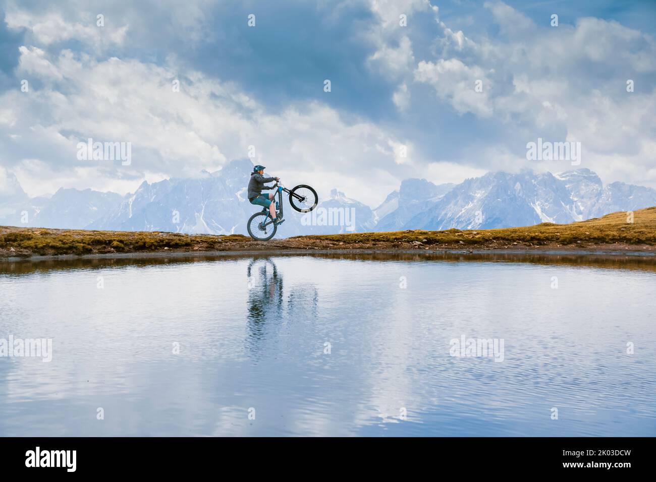Italie, Tyrol du Sud, Bolzano / Bozen, San Candido / Innichen. Cavalier avec e-bike, réflexion dans un petit lac alpin en une journée nuageux Banque D'Images