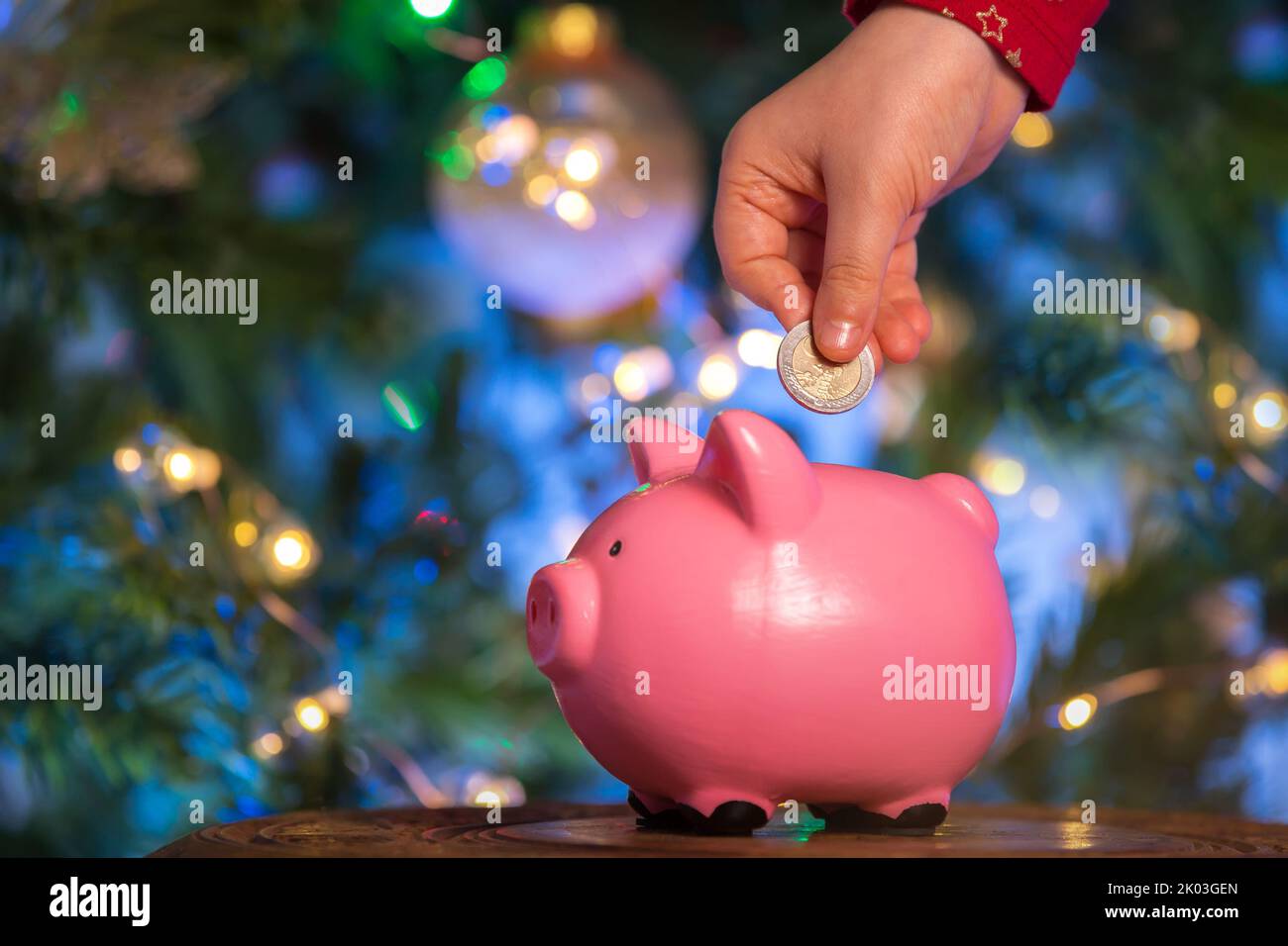 Les mains des enfants mettent une pièce dans une banque de porc rose sur un fond de bokeh du nouvel an. Le concept d'investissement dans l'avenir de l'enfant, l'épargne, fina Banque D'Images