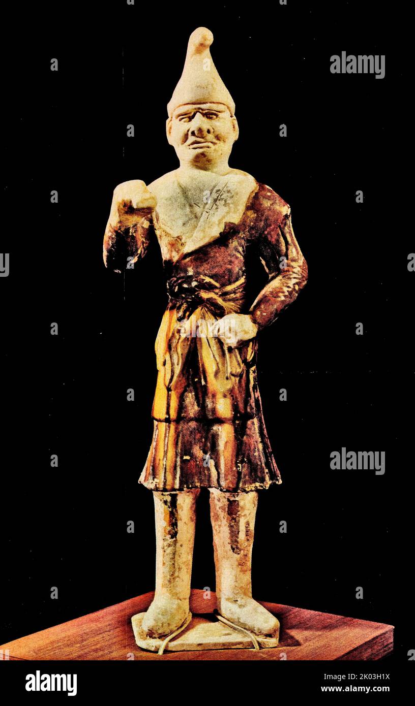Figurine blanche Tang Dynasty, debout obliquement sur une petite plaque plate, portant un chapeau Hu pointu, ressemblant à un homme Hu. Il avait un nez haut, des yeux levés, une barbe complète et une expression sérieuse. Il porte un grand peignoir à barbe avec un grand revers, des manches étroites, une ceinture et des bottes hautes. Il fait des poings des deux mains. Tout le corps est peint avec du glaçure jaune, le lapel est un glaçure jaune clair, le chapeau et la tête des figurines n'ont pas été vitrés à l'origine, seulement un peu de glaçure jaune a été peint sur la joue droite, qui peut être intentionnel par le potier. Ses vêtements et sa posture sont semblables à t Banque D'Images