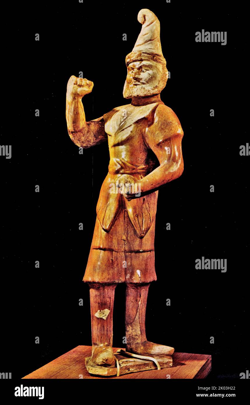 Figurine blanche Tang Dynasty, debout obliquement sur une petite plaque plate, portant un chapeau Hu pointu, ressemblant à un homme Hu. Il avait un nez haut, des yeux levés, une barbe complète et une expression sérieuse. Il porte un grand peignoir à barbe avec un grand revers, des manches étroites, une ceinture et des bottes hautes. Il fait des poings des deux mains. Tout le corps est peint avec du glaçure jaune, le lapel est un glaçure jaune clair, le chapeau et la tête des figurines n'ont pas été vitrés à l'origine, seulement un peu de glaçure jaune a été peint sur la joue droite, qui peut être intentionnel par le potier. Ses vêtements et sa posture sont semblables à t Banque D'Images