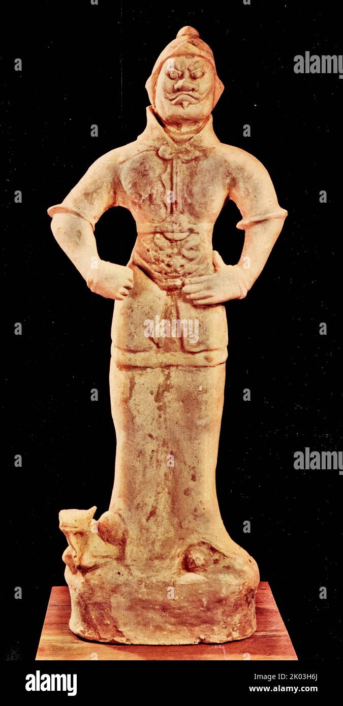 Tang Figurine; debout. Son corps en argile est blanc, et il y a des traces de couleurs rouges et noires peintes et de poudre blanche. Cette figurine a des cheveux sur le dessus de sa tête, porte une chemise à manches courtes et à col haut, un manteau d'armure, un casque de bête sur ses épaules et sa poitrine, ses pieds légèrement écartés, et il se tient sur une plate-forme qui a été détruite. La tête de cette figurine est étirée tout droit, ses sourcils soulevés, sa bouche largement ouverte, et ses cheveux sur les temples séparés de gauche à droite. La main droite tient une arme. Il ressemble à un peuple Hu, et son apparence est assez audacieuse. Banque D'Images