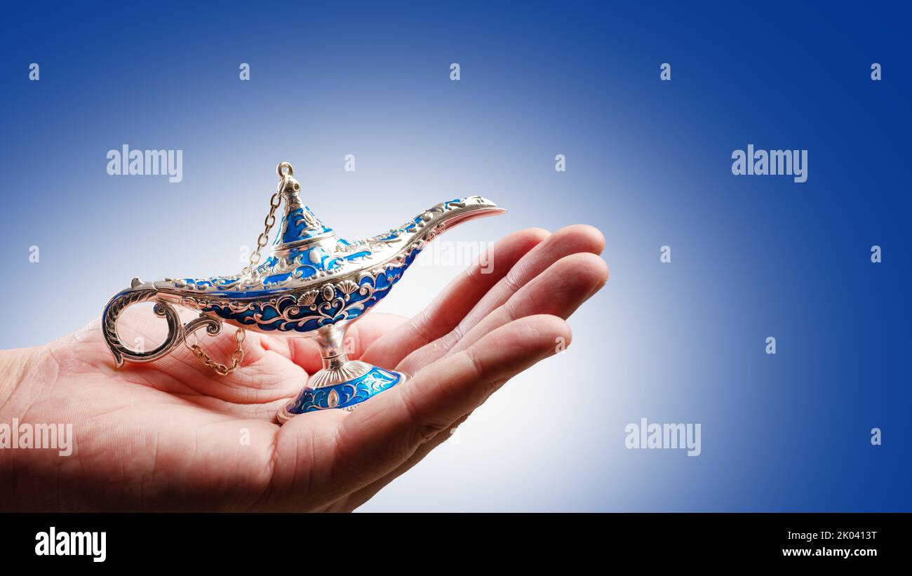 Lampe magique d'Aladdin dans la main d'une femme sur fond bleu pâle. Contes de fées arabes, magie. Symbole de bonne chance, richesse. Publicité, bannière, invita Banque D'Images