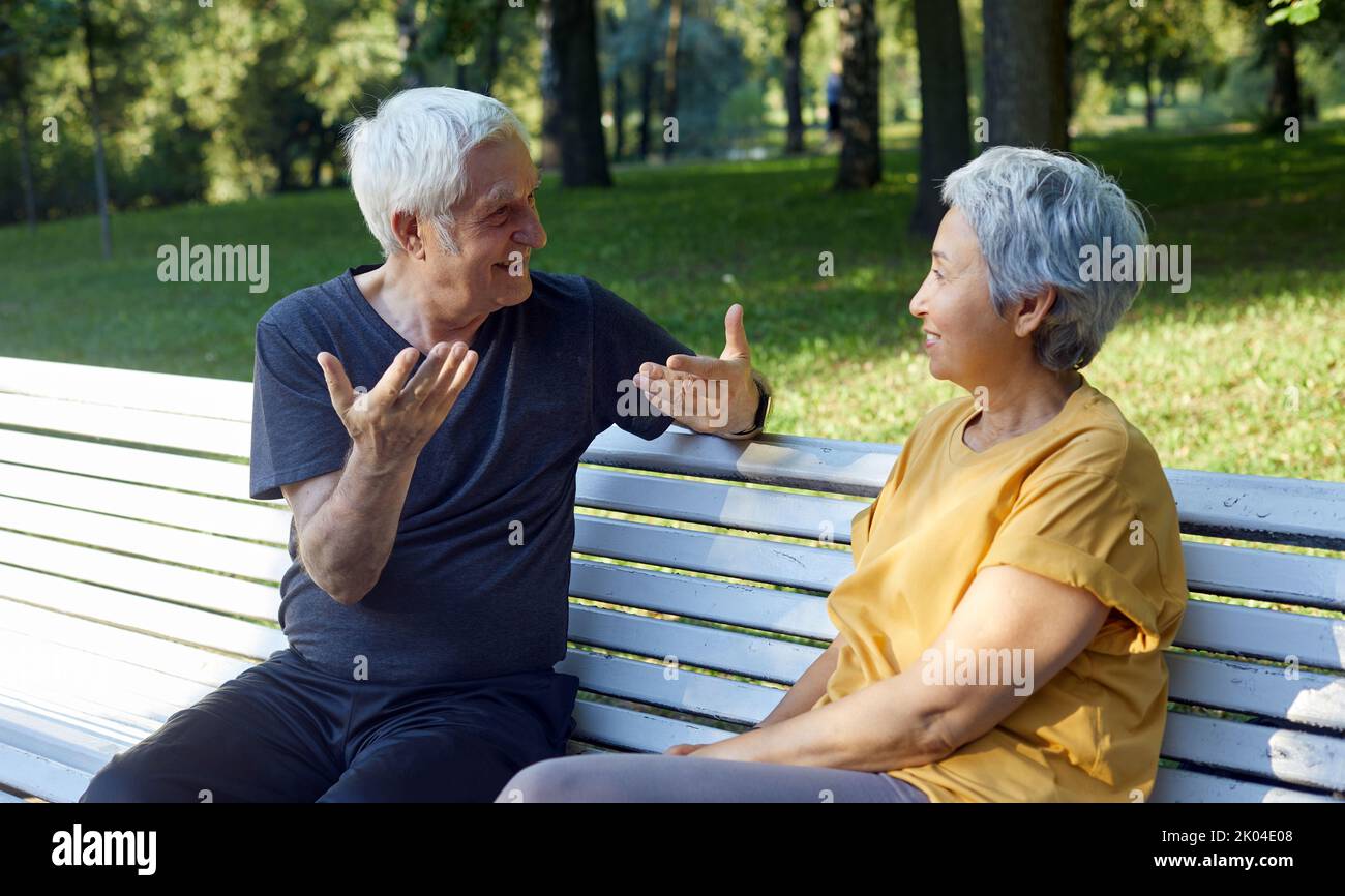 Les conjoints multiethniques des couples seniors sont assis sur le banc. Profitez d'une discussion dans le parc public d'été en discutant avec un ami et partagez vos pensées ou vos nouvelles pendant les repas Banque D'Images