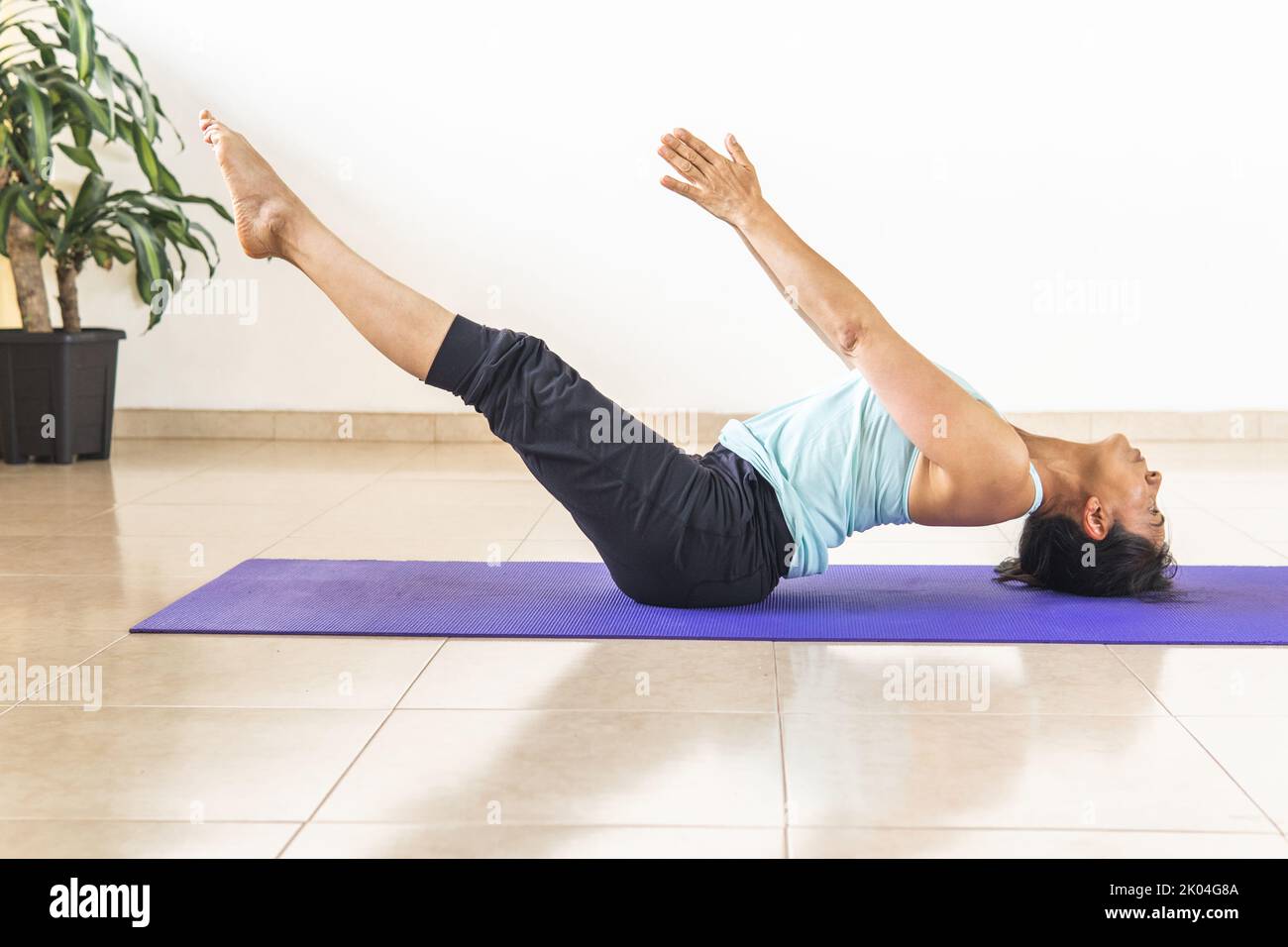 Latino-femme pratique le yoga, Uttana padasana posture couché sur son dos en se penchant sur sa tête et les fesses avec ses jambes et les bras étendus sur un tapis Banque D'Images
