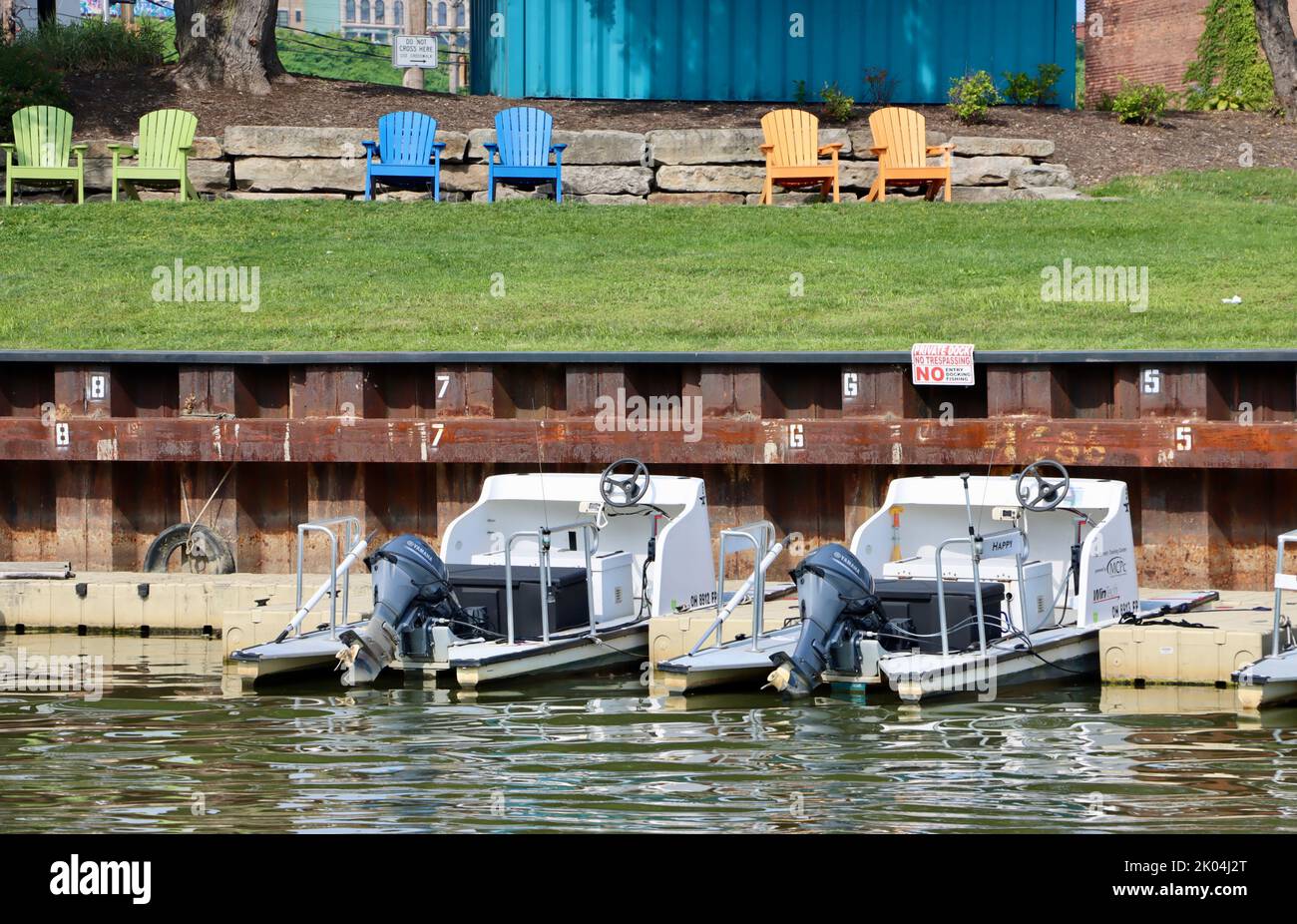 Chaises Adirondack sur la pelouse au bord de la rivière avec des bateaux à quai. Banque D'Images