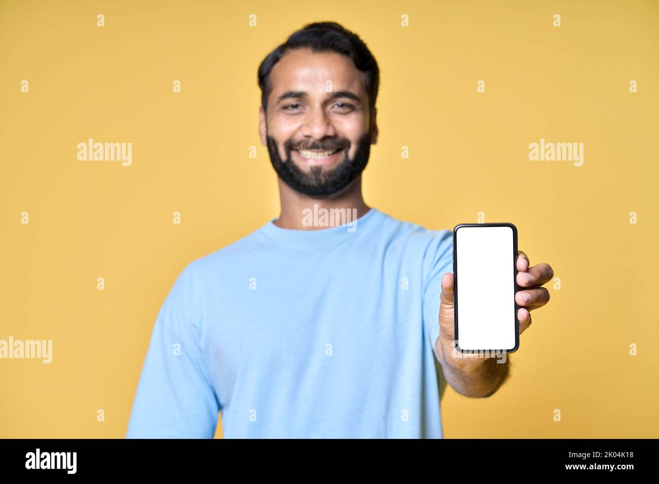 Un Indien heureux montrant un téléphone mobile pointant vers l'écran isolé sur jaune. Banque D'Images