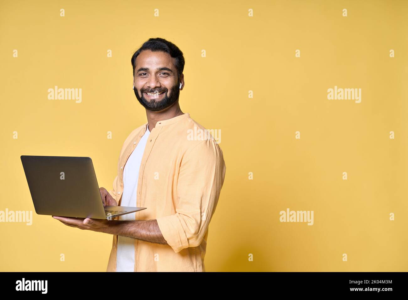 Un homme d'affaires indien heureux étudiant tenant un ordinateur portable isolé sur jaune. Banque D'Images