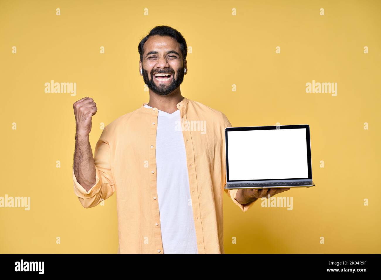Un Indien heureux célébrant la victoire montrant un écran d'ordinateur portable isolé sur jaune. Banque D'Images