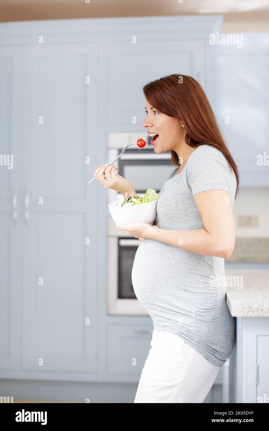 Les soins que le bébé mérite. Une femme enceinte qui mange une salade saine dans la cuisine - CopySpace. Banque D'Images