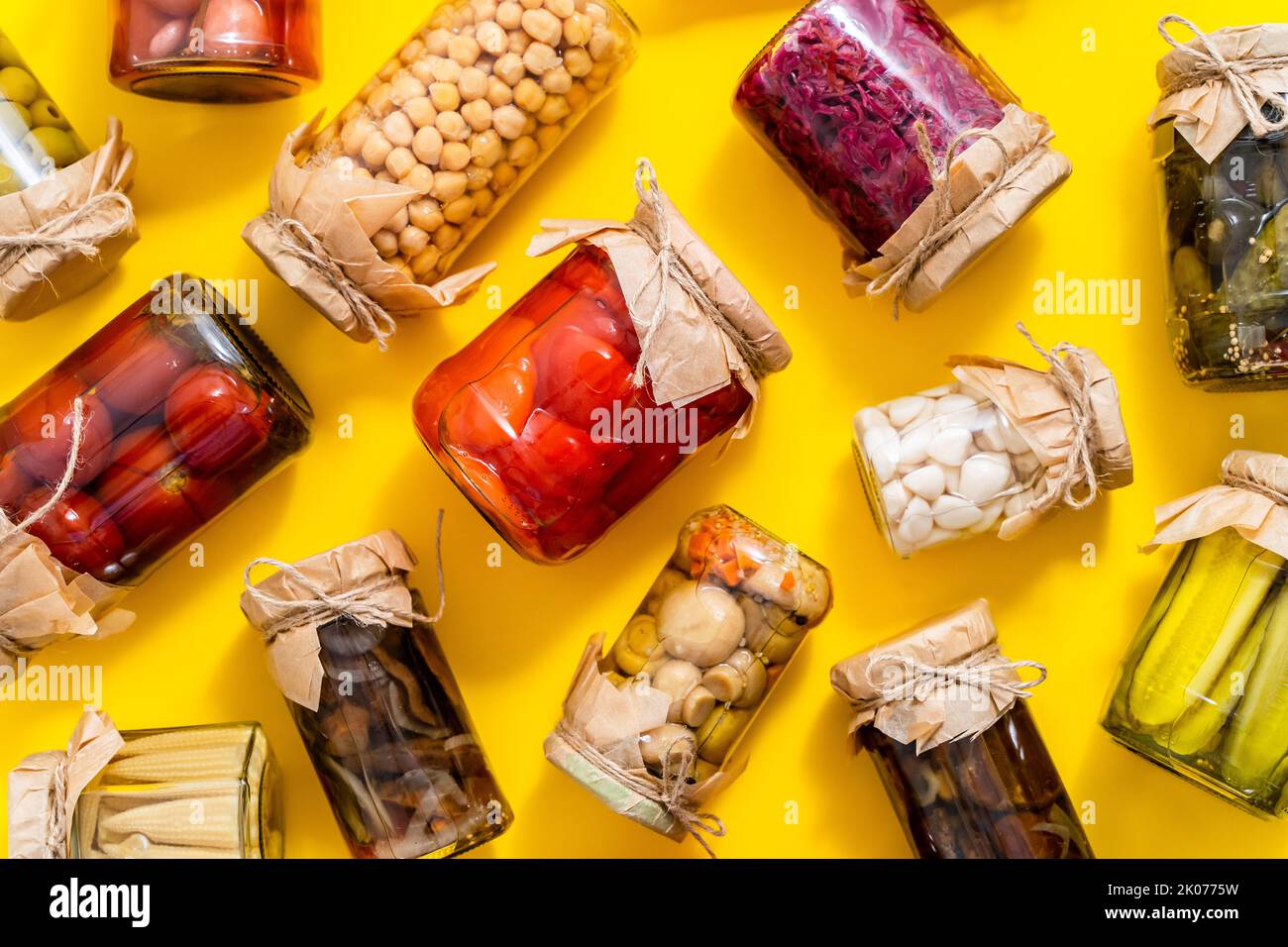 Divers types préserve les légumes et les champignons dans des pots en verre. Placé sur fond jaune Banque D'Images