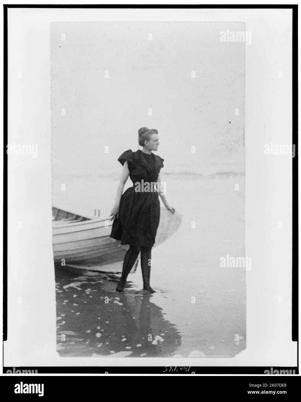 Frances Benjamin Johnston, portrait pleine longueur, debout au bord de l'océan, en maillot de bain, avec la main gauche sur le bateau, vers la droite, entre 1880 et 1900. Banque D'Images