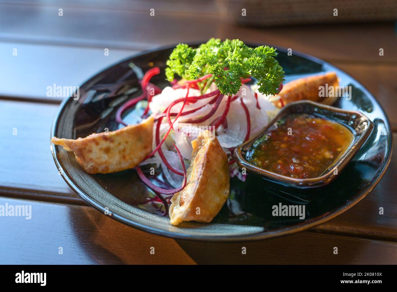 Gyoza frits, servi avec une sauce aigre-douce épicée et une salade comme plat de hors-d'œuvre sur une assiette noire, cuisine asiatique sur une table en bois, espace de photocopie, sélection Banque D'Images