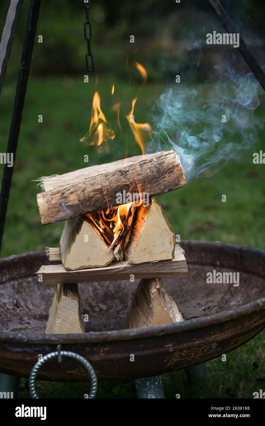 Bois de bois de chauffage en rondins arrangée avec des flammes et de la fumée dans un foyer sous un tripode grill dans un jardin pour une fête de barbecue, copie spa Banque D'Images