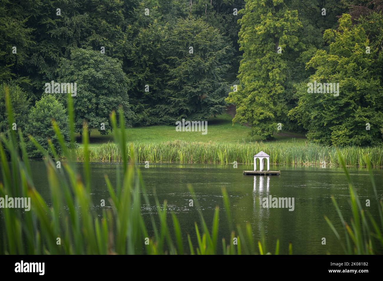 Petite île artificielle avec un pavillon blanc pour les oiseaux aquatiques sur le lac dans le parc idyllique de Putbus avec des roseaux à la rive, grand vieux tre Banque D'Images