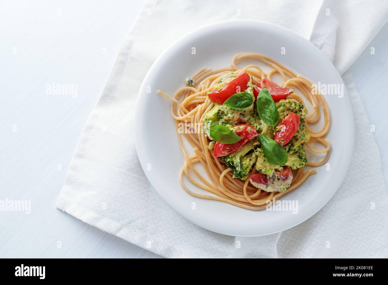 Spaghetti aux grains entiers avec sauce à la crème de brocoli, garniture de tomates et de basilic sur une assiette blanche, repas végétarien sain, espace de copie, vue du dessus, Banque D'Images
