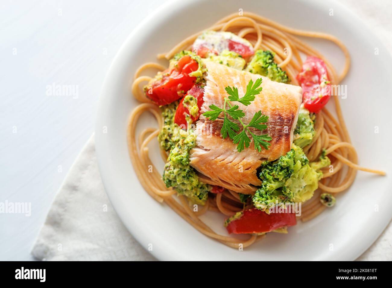 Filet de saumon sauvage sur des spaghettis de grains entiers avec brocoli, tomates et garniture de persil, repas sain sur une assiette blanche, rythme de copie, vue de haut angle fro Banque D'Images