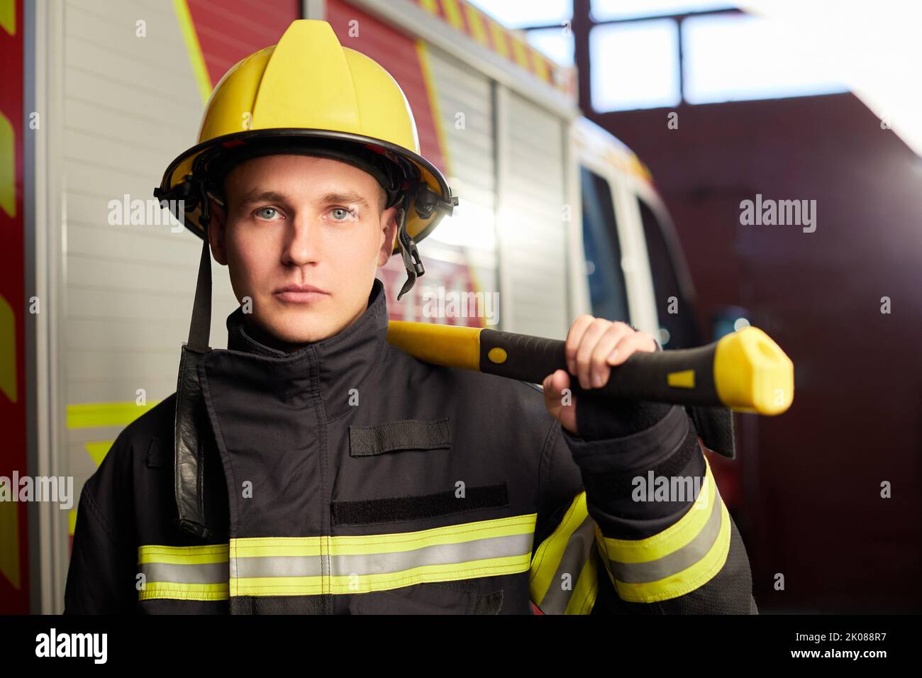 Pompier entièrement équipé avec casque et hache en arrière-plan de camion de feu. Banque D'Images