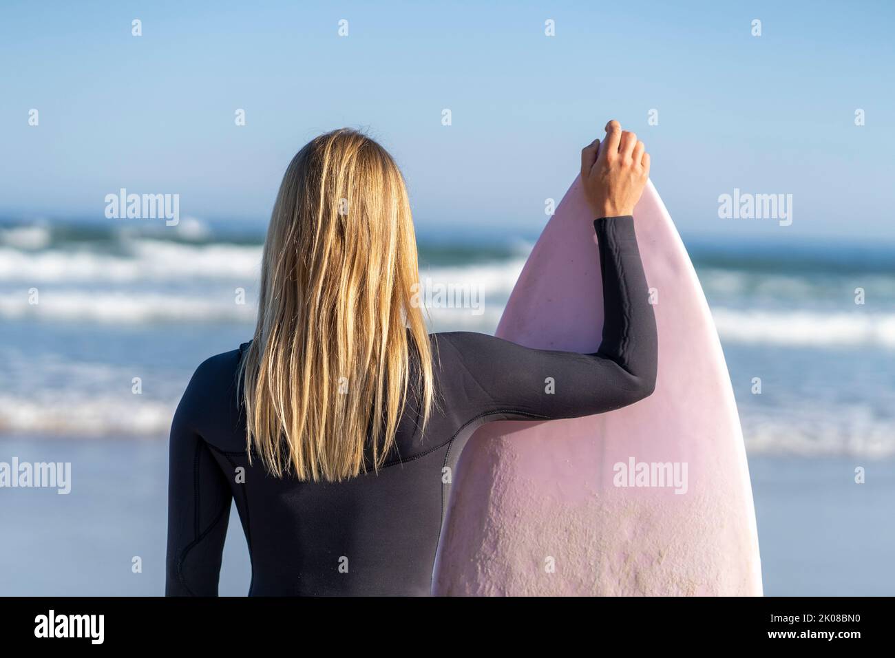 Surfeuse fille à la plage regardant les vagues avec sa planche de surf. Femme surfeuse Banque D'Images