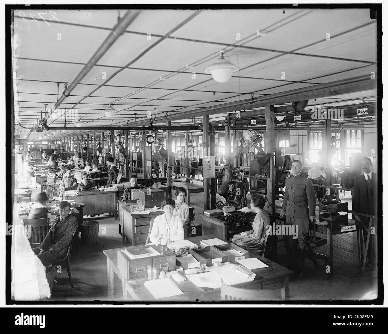Division de la formation, entre 1910 et 1920. Travailleuses de bureau, États-Unis. Notez les ventilateurs électriques. L'avis se lit comme suit : « instructions d'entretien, Globe Automatic sprinkleur Company ». Officier DE l'armée AMÉRICAINE par des plateaux en bois marqués 'Telegrams'. Banque D'Images