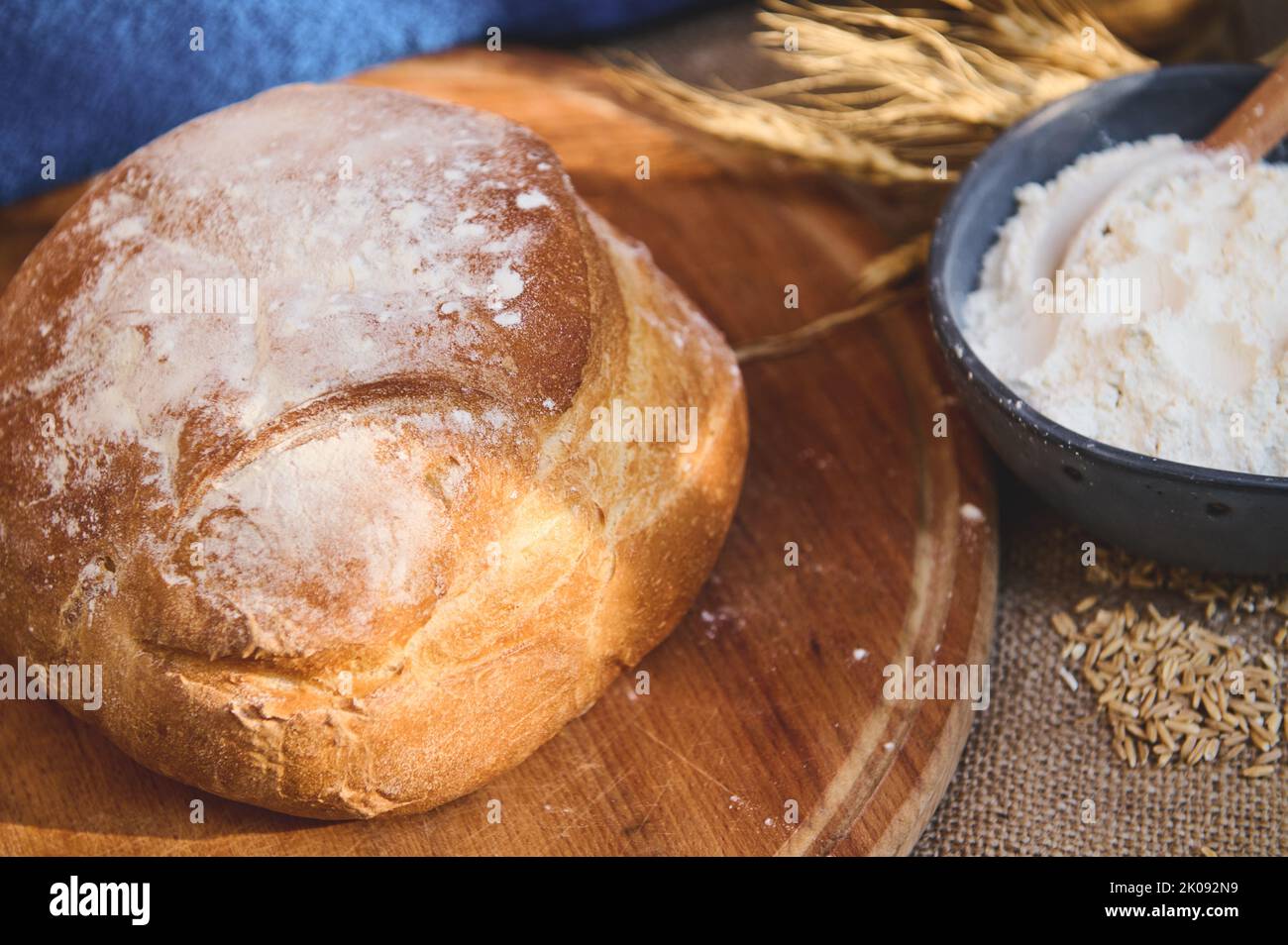 Un pain de levain sur une planche de bois, sur un bol en céramique bleu avec farine blanche et épillets de blé Banque D'Images